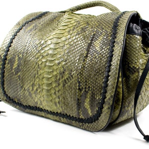 Könnte beinhalten: Eine grüne und schwarze Handtasche mit Schlangenmuster, mit einem oberen Griff und Kordelzugverschluss. Die Tasche hat schwarze geflochtene Zierleisten und schwarze Kordelzüge. Die Tasche ist aus einem strukturierten Material gefertigt.
