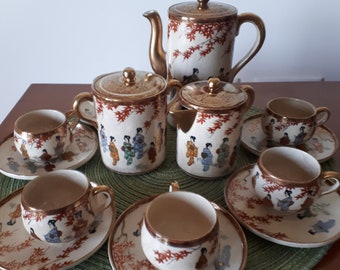 May include: A vintage Japanese tea set with a white background and gold accents. The set includes a teapot, creamer, sugar bowl, and four cups and saucers. The cups and saucers feature a floral design with a gold rim.