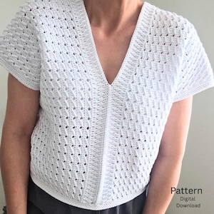 May include: A white short-sleeved top featuring a textured crochet pattern with a deep V-neckline and a vertical ribbed center panel. The garment has a structured border along the neckline and hem. The image includes the text Pattern Digital Download.