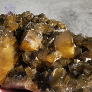 Puede incluir: Un cúmulo de cristales de barita de color marrón dorado con un aspecto facetado y afilado. Los cristales están dispuestos en un patrón aleatorio y natural, creando una exhibición única e interesante.