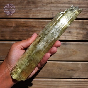 May include: A large, light green, translucent, striated, crystal point. The crystal is about 10 inches long and has a rough, natural finish.