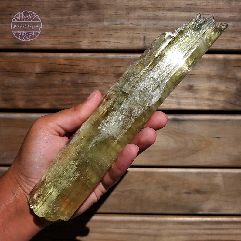 May include: A large, light green, translucent, striated, crystal point. The crystal is about 10 inches long and has a rough, natural finish.