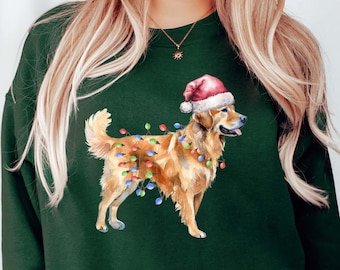 Op de afbeelding: Een groen sweatshirt met een golden retriever die een kerstmanmuts en kerstverlichting draagt. De hond staat op een groene achtergrond.