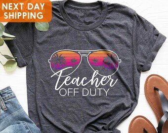 May include: A dark gray t-shirt with a white graphic of sunglasses with palm trees reflected in the lenses. The text "Teacher Off Duty" is below the sunglasses.