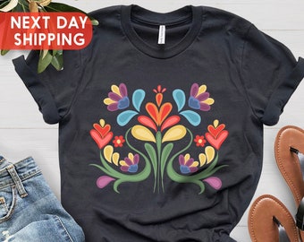 May include: Black t-shirt with a colorful floral design. The design features a variety of flowers and leaves in shades of red, yellow, blue, green, and purple.