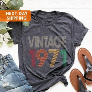 May include: A dark grey t-shirt with the text "Vintage 1971" in colourful retro-style font.