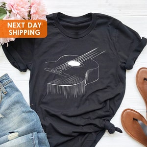 May include: Black t-shirt with a white outline of an acoustic guitar. The guitar is positioned horizontally across the shirt.