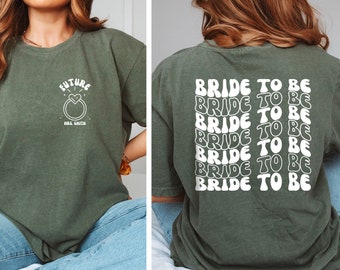May include: A green t-shirt with a white graphic on the front that says "Future Mrs. Smith" with a ring and heart design. The back of the shirt has the text "Bride to Be" repeated six times in a retro font.