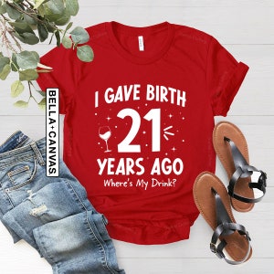 May include: Red t-shirt with white text that reads "I gave birth 21 years ago. Where's my drink?"  A wine glass icon is next to the number 21.