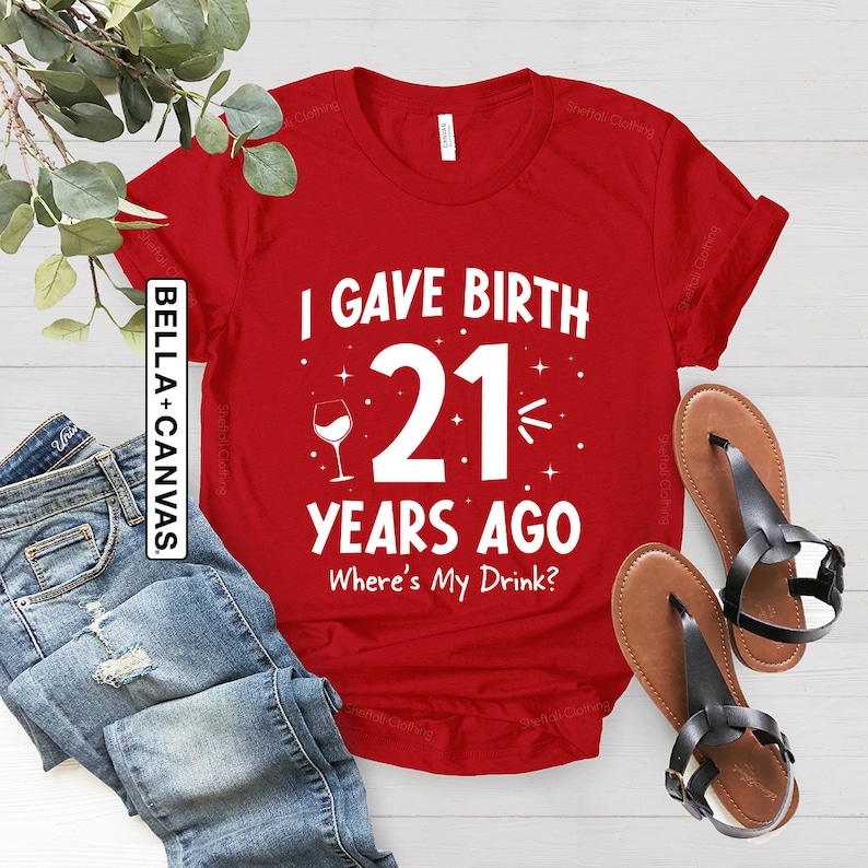 May include: Red t-shirt with white text that reads "I gave birth 21 years ago. Where's my drink?"  A wine glass icon is next to the number 21.