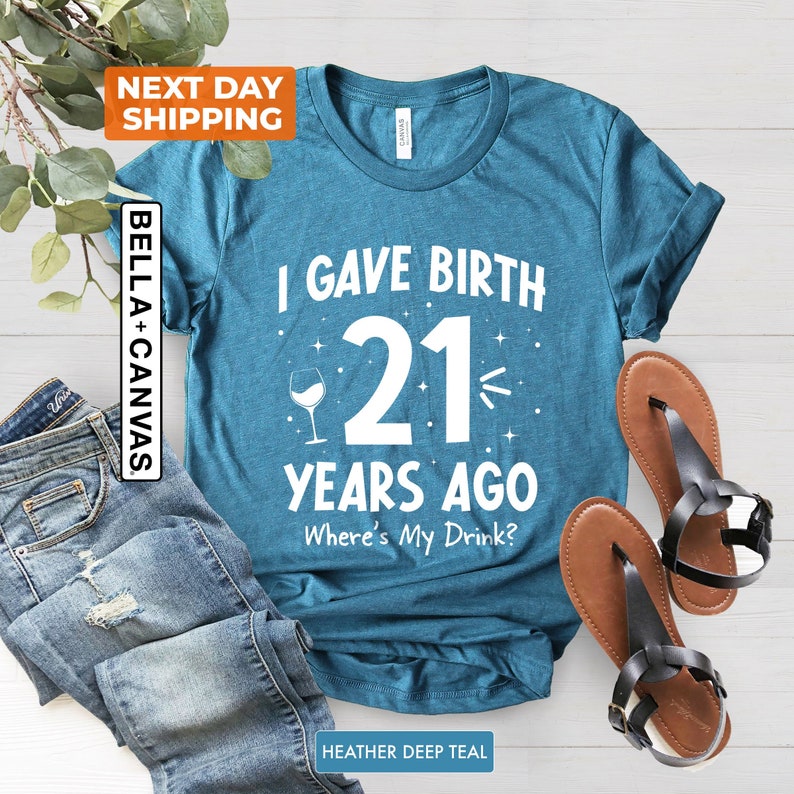 May include: A teal blue t-shirt with the text "I gave birth 21 years ago Where's My Drink?" in white. A wine glass icon is next to the number 21.