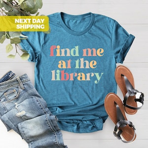 Puede incluir: Una camiseta azul turquesa con el texto "find me at the library" en colores arco&iacute;ris. El texto est&aacute; en una fuente divertida y casual.