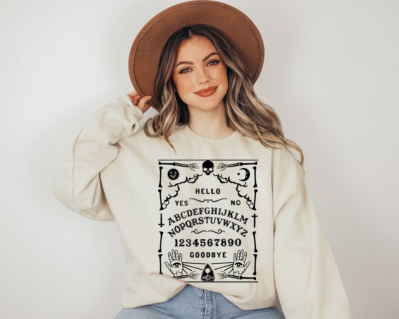 May include: A cream-coloured sweatshirt with a black and white Ouija board design. The design includes the words "Hello", "Goodbye", "Yes", "No", and the letters of the alphabet.