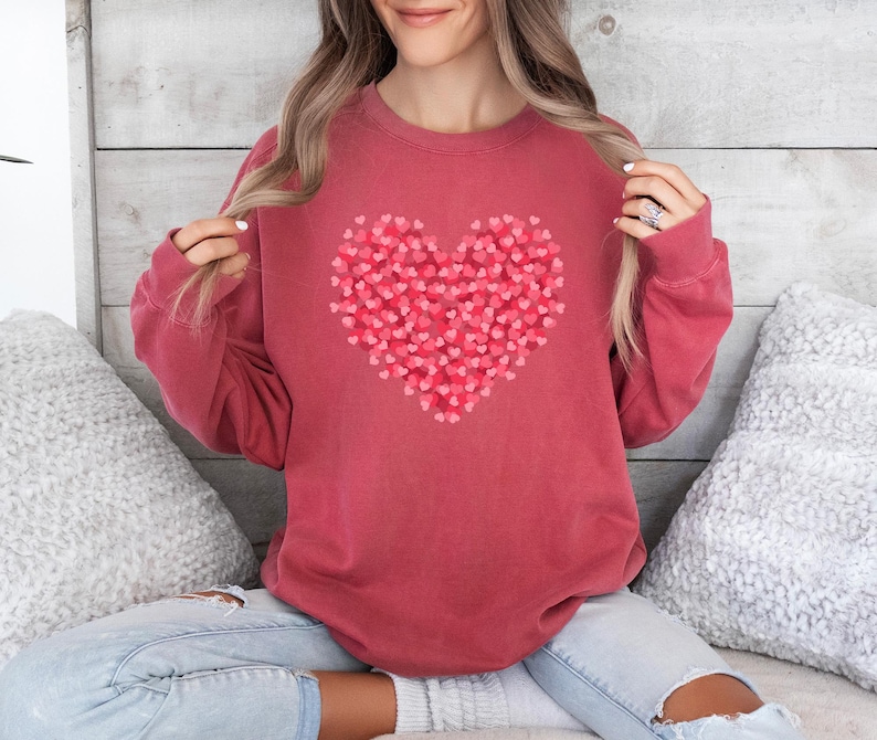 May include: A red sweatshirt with a large heart design made up of smaller pink hearts.