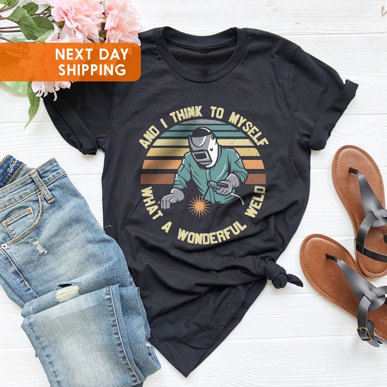 Puede incluir: Camiseta negra con un gr&aacute;fico retro de un soldador con el texto "And I think to myself what a wonderful weld".