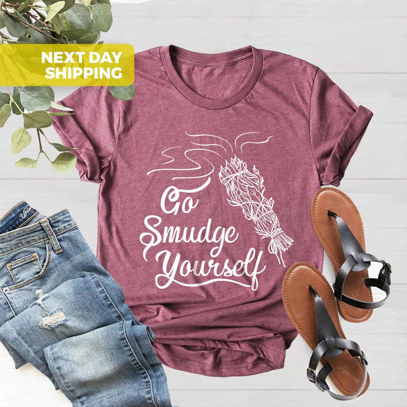May include: A maroon t-shirt with a white graphic of a smudge stick with smoke and the text "Go Smudge Yourself".