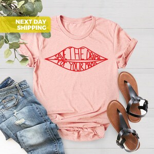 K&ouml;nnte beinhalten: Ein rosa T-Shirt mit einem roten Umriss einer Lippenpartie. Der Text innerhalb der Lippen lautet "Save the drama for your mama."