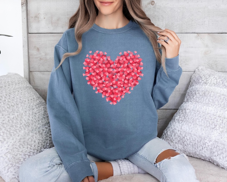 May include: A blue sweatshirt with a large heart design made up of smaller pink hearts.