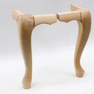 May include: Two unfinished wooden table legs with a curved design. The legs are made of light wood and are ready to be stained or painted.