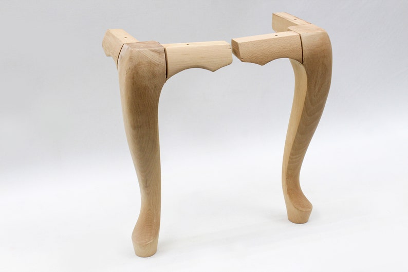 May include: Two unfinished wooden table legs with a curved design. The legs are made of light wood and are ready to be stained or painted.