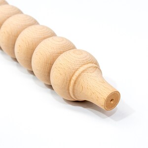 May include: A close-up of a wooden furniture leg with a rounded, beaded design. The leg is unfinished and has a natural wood color.