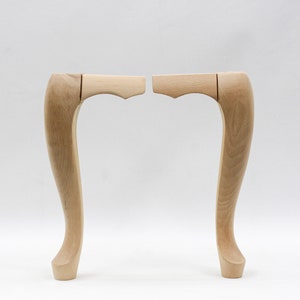 May include: Two unfinished wooden chair legs with a curved design. The legs are made of light-colored wood and have a smooth finish.
