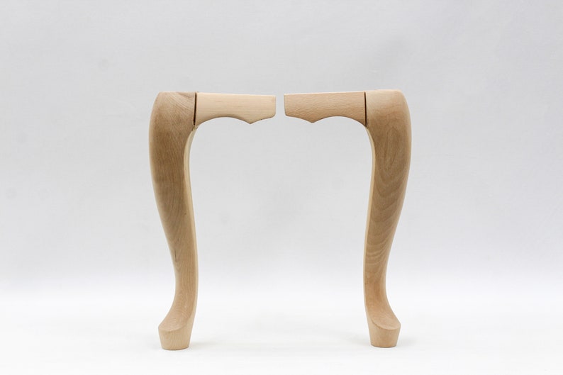 May include: Two unfinished wooden chair legs with a curved design. The legs are made of light-colored wood and have a smooth finish.