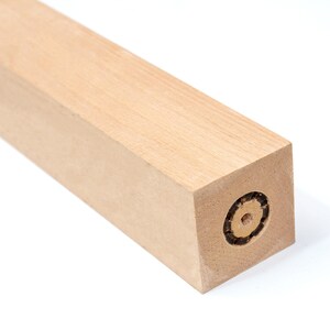 May include: A close-up of a wooden furniture leg with a square end. The end of the leg has a circular hole with a threaded insert.
