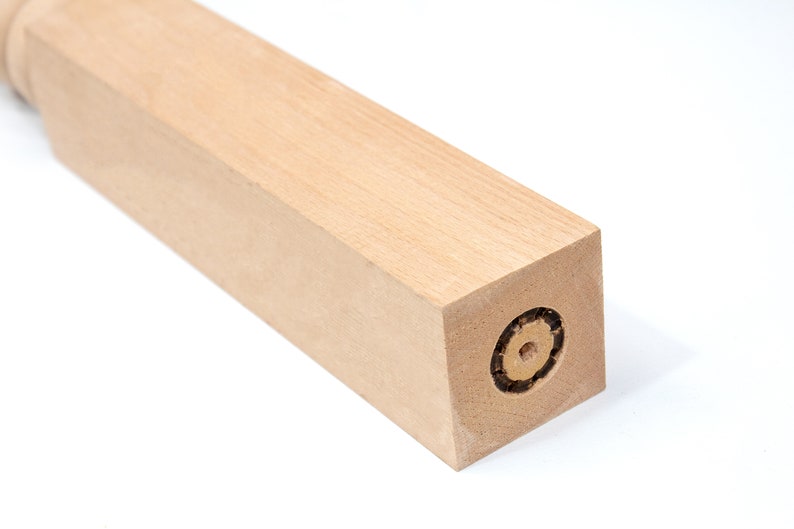 May include: A close-up of a wooden furniture leg with a square end. The end of the leg has a circular hole with a threaded insert.