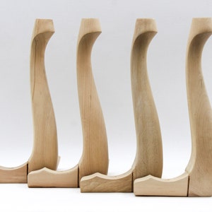 May include: Four unfinished wooden chair legs with a curved design. The legs are arranged in a row from left to right.