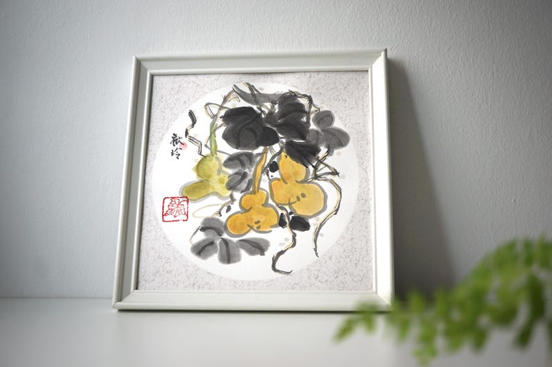 May include: A framed watercolor painting featuring a gourd and vine design. The artwork showcases yellow gourds, dark gray leaves, and stems against a white circular background. The frame is white, and the painting has Chinese characters and a red stamp.
