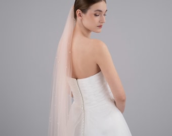 May include: A bride wearing a white strapless wedding dress with a blush pink veil with pearl accents.