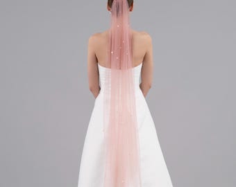 May include: A long, blush-colored tulle veil with pearl embellishments. The veil is worn by a person with their back to the camera.