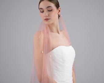 May include: A blush pink bridal veil with pearl embellishments. The veil is made of soft tulle and is perfect for a romantic wedding.