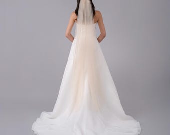 May include: A white bridal veil with a blush colored tulle overlay. The veil is worn by a person with long dark hair. The veil is long and flows down the back of the person.