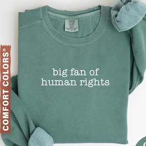 Könnte beinhalten: Hellgrünes Sweatshirt mit dem weißen Text "big fan of human rights". Es hat einen Rundhalsausschnitt und lange Ärmel mit weichen, strukturierten Bündchen. Die Worte "Comfort Colors" sind auf einem braunen Etikett aufgedruckt.