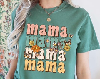 May include: A green t-shirt with the text "mama" repeated four times in a stacked, retro design. Each "mama" is a different color, with pink, blue, yellow, and orange. The shirt has a floral and butterfly pattern.