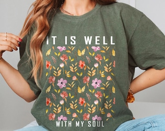 May include: A green t-shirt with a floral pattern and the text "It is well with my soul" printed on the front.