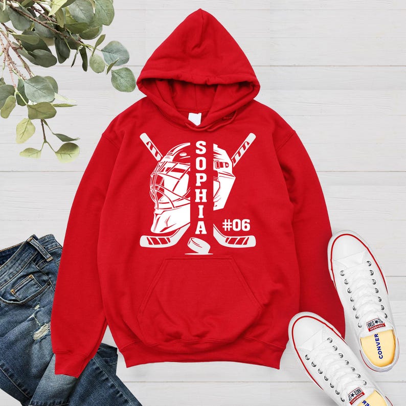 May include: Red hoodie with a white hockey goalie mask and sticks design. The text "Sophia #06" is printed on the hoodie.