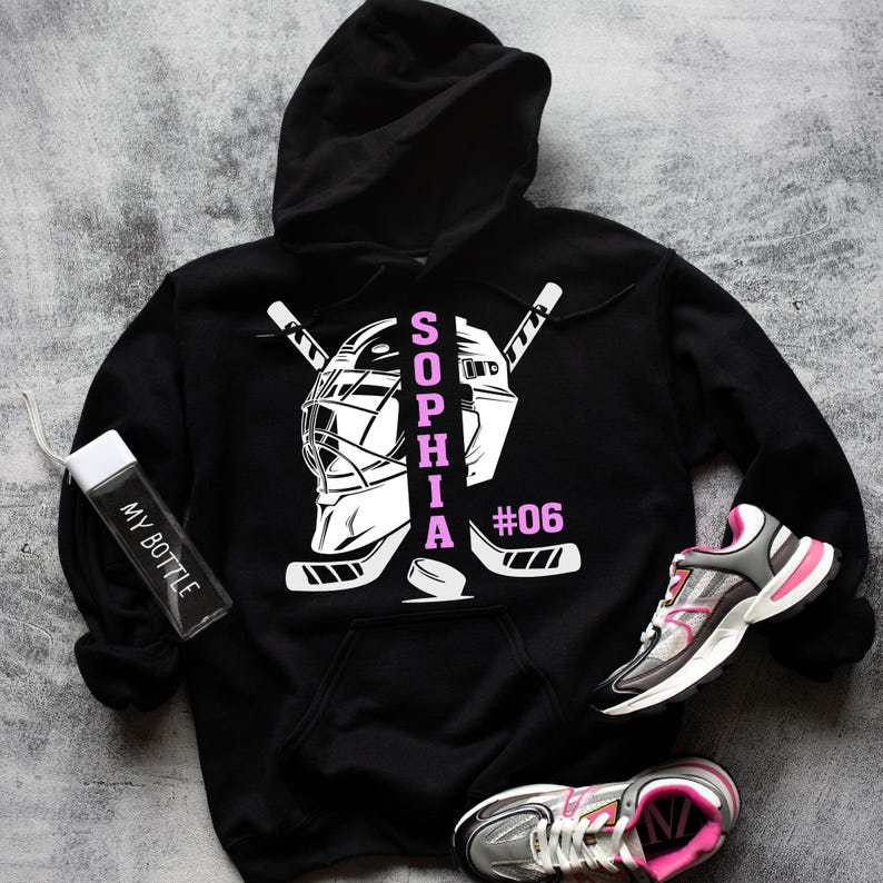 May include: Black hoodie with a white hockey goalie mask and crossed hockey sticks. The name "SOPHIA" is written vertically in pink letters and the number "#06" is written in white.