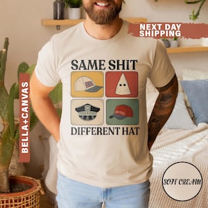 May include: A cream-coloured t-shirt featuring the text "SAME SHIT DIFFERENT HAT" above four images of different hats. The images include a baseball cap, a KKK hood, a police hat, and a red baseball cap.