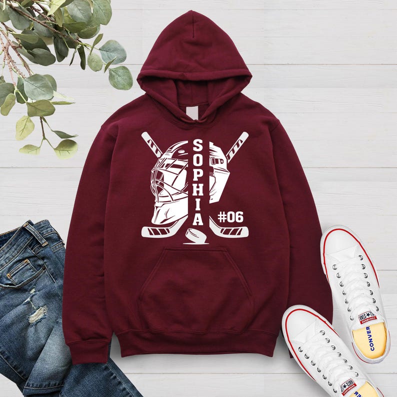 May include: Burgundy hoodie with a white hockey goalie mask and crossed hockey sticks. The text "SOPHIA #06" is printed on the hoodie.