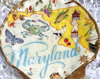 May include: A decorative seashell with a hand-painted map of Maryland. The map features a blue crab, a butterfly, and the word "Maryland" in blue script. The shell has a gold-painted edge.