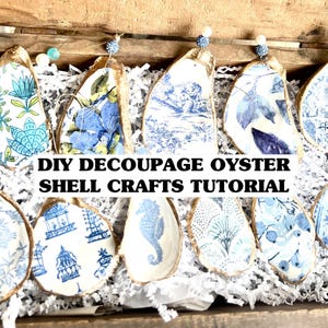 Op de afbeelding: DIY decoupage oester schelp knutsel tutorial. Een close-up van verschillende oesterschelpen versierd met blauw-wit gepatroneerd papier. De schelpen hangen aan een touwtje en worden getoond op een bed van wit gescheurd papier.