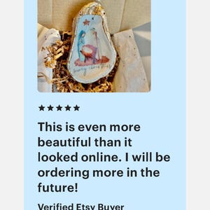 May include: A white, pear-shaped ornament with a painted image of the nativity scene and the text "Merry Christmas".