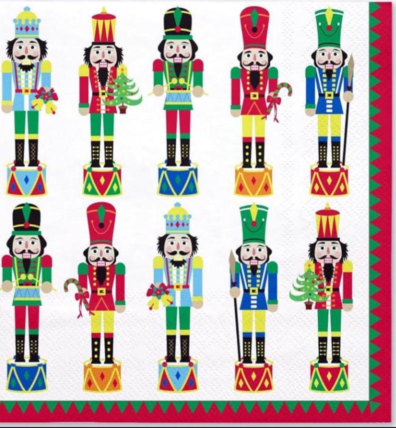 May include: A white napkin featuring a repeating pattern of colorful nutcracker soldiers. Each nutcracker is dressed in a different uniform, with details like hats, jackets, and accessories in red, green, blue, and yellow. The napkin has a red and green border.