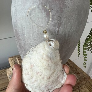 May include: A white seashell with a gold and pearl accent hanging from a thin gold wire.