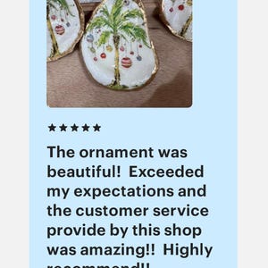 May include: Three oyster shell ornaments with gold trim, each painted with a palm tree and colorful Christmas ornaments. The ornament in the center is the largest and features a green palm tree with red, green, yellow, and white ornaments.