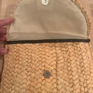 以下が含まれることがあります： マグネット開閉式の編み込みストロークラッチ。内側は薄いベージュ色の生地で裏打ちされています。クラッチは丸みを帯びたフラップと濃い茶色のトリムが付いています。マグネット開閉部はシルバーです。