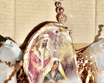 May include: A gold-painted oyster shell ornament with a nativity scene image inside. The ornament has a wire loop and gold beads for hanging.